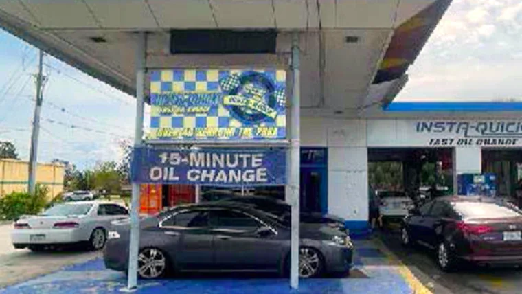 Cars parked at an oil change service station with a sign advertising "15-Minute Oil Change" under a covered area.