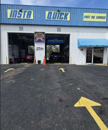 Exterior view of an Insta Quick Fast Oil Change service center with three garage bays and yellow directional arrows on the asphalt.