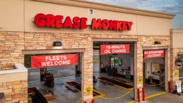 A Grease Monkey auto service center with open garage bays, signs reading "Fleets Welcome," "15-Minute Oil Change," and "No Appointment Necessary.