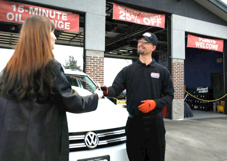 A Grease Monkey mechanic standing in front of three bay doors handing a woman a set of keys.