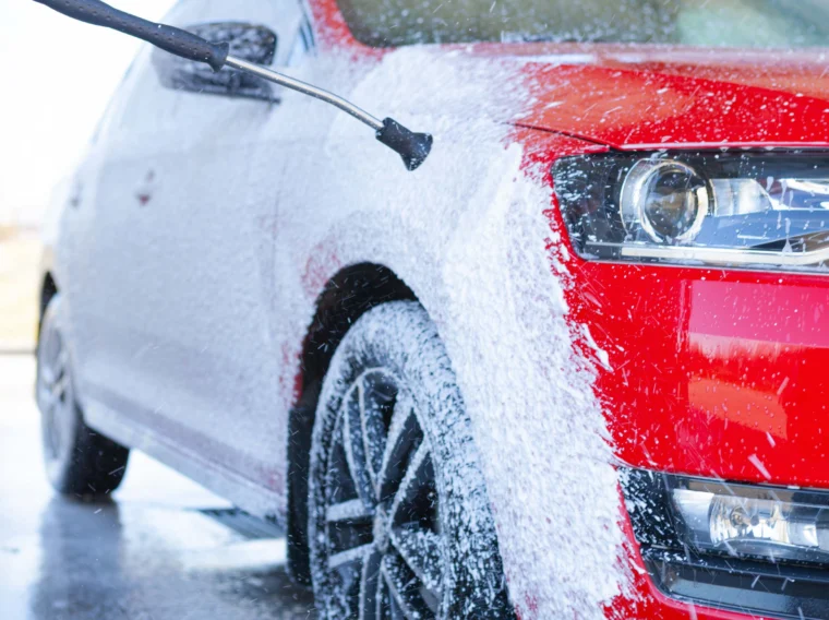 A red car getting washed with soapy water from a pressure washer