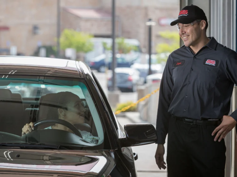 A person in a car speaks with a smiling service worker in uniform standing outside a building entrance, ready to assist with expert car detailing.