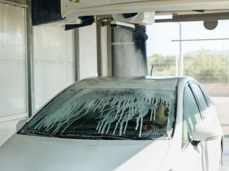 A car getting washed with a woman inside of the vehicle.