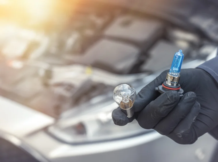 A hand holding two light bulbs of a car headlight.