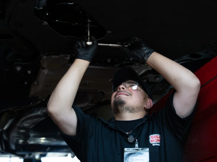A mechanic wearing gloves, safety glasses, and a uniform works underneath a raised vehicle with a wrench, performing essential filter services.