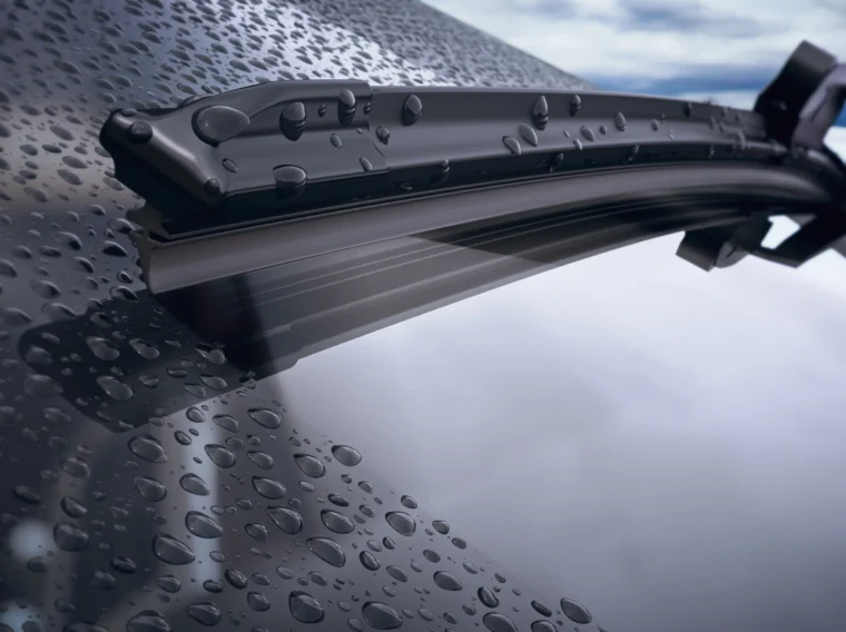 A closeup of a car's windshield and wiper blade with rain drops