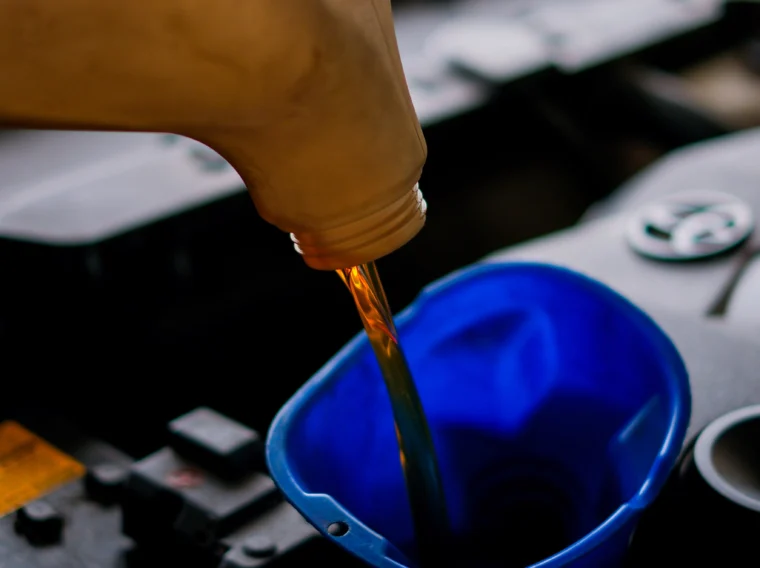 Motor oil is being poured from a plastic container into a blue funnel placed in a car engine compartment during Fluid Exchange Services.