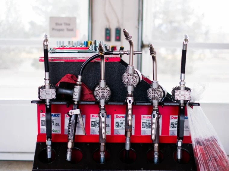 A row of oil dispensing nozzles mounted above oil containers and tools in a garage, ready for efficient Fluid Exchange Services in a service station setting.
