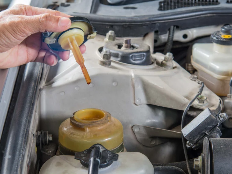 A hand holding a cap to a power steering reservoir.
