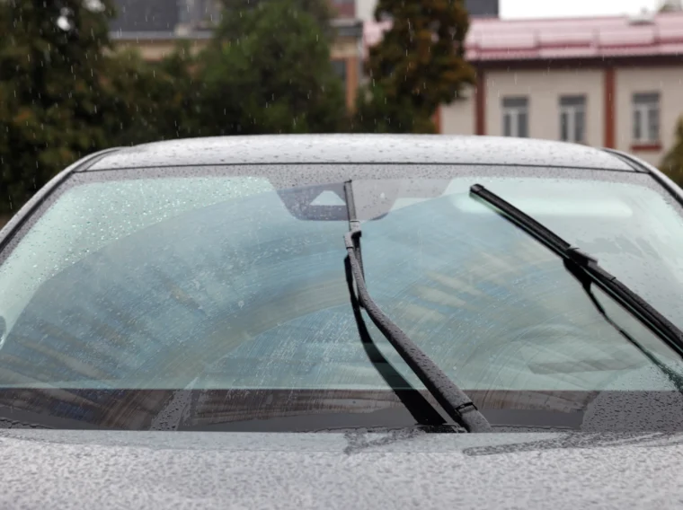 Car wiper blades cleaning water drops off a windshield.