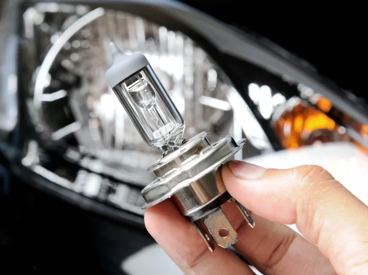 A hand holding a car's headlight bulb.