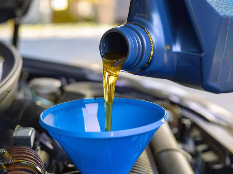 Motor oil is being poured from a blue container into a blue funnel placed in a car engine compartment during top maintenance services.