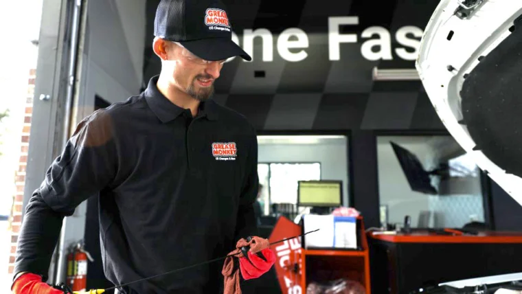 Grease Monkey mechanic holding a dipstick while checking engine oil.