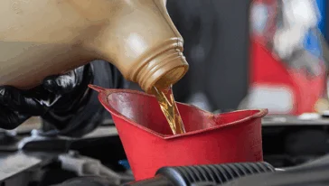 Oil being poured into a funnel placed in an engine’s oil fill port.