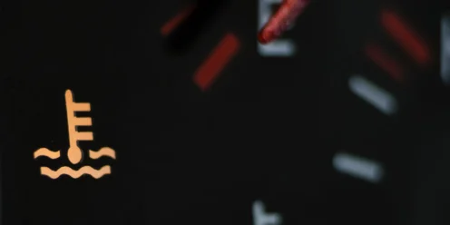 Close-up of a car dashboard warning light showing the engine temperature symbol, alerting the driver to possible engine overheating.
