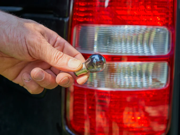 A hand holding a light bulb in front of a vehicle's taillights.