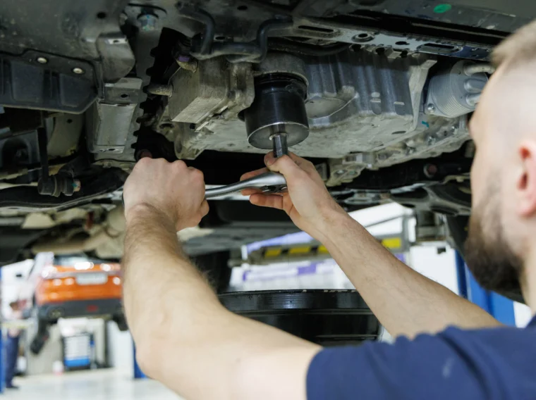 A mechanic underneath a vehicle replacing a filter.