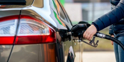 A person is refueling a car at a gas station, holding a fuel nozzle inserted into the vehicle’s fuel tank to increase fuel efficiency on their next drive.