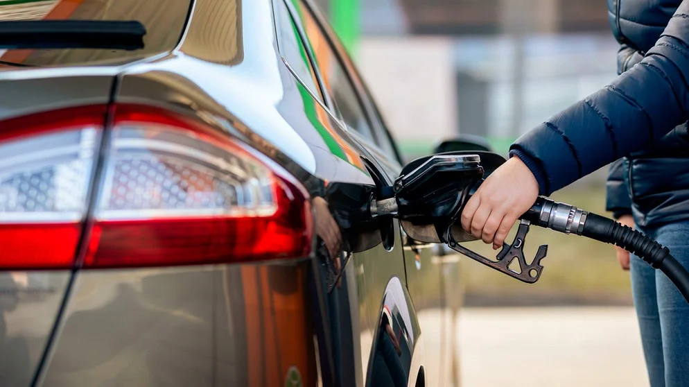 A person is refueling a car at a gas station, holding a fuel nozzle inserted into the vehicle’s fuel tank to increase fuel efficiency on their next drive.