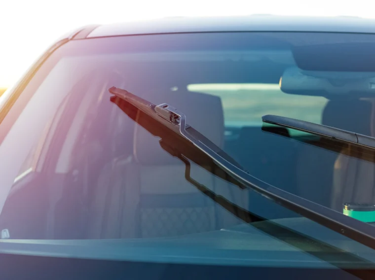 Close-up view of a car windshield with two wipers, showing the interior in the background—perfect for illustrating wiper replacement or wiper blade replacement services.